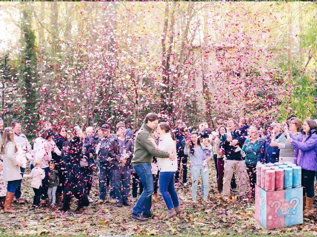 Family and friends gathered around pregnant couple setting off pink gender reveal confetti cannons.