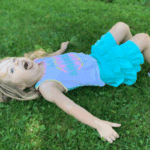 Strong-willed child lying on the grass with a dramatic expression during a toddler meltdown moment.