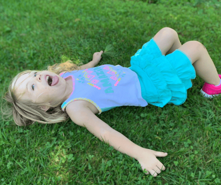 Strong-willed child lying on the grass with a dramatic expression during a toddler meltdown moment.