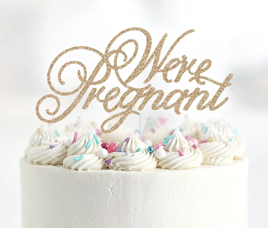 “We’re pregnant” cake topper on a white cake with sprinkles.