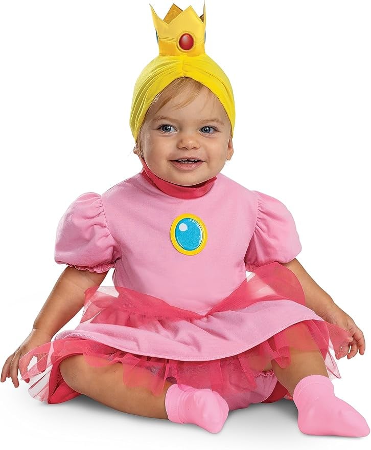 Smiling baby in a pink Princess Peach costume with puff sleeves, tulle skirt, and a yellow crown headband — adorable toddler outfit for a Super Mario family Halloween theme