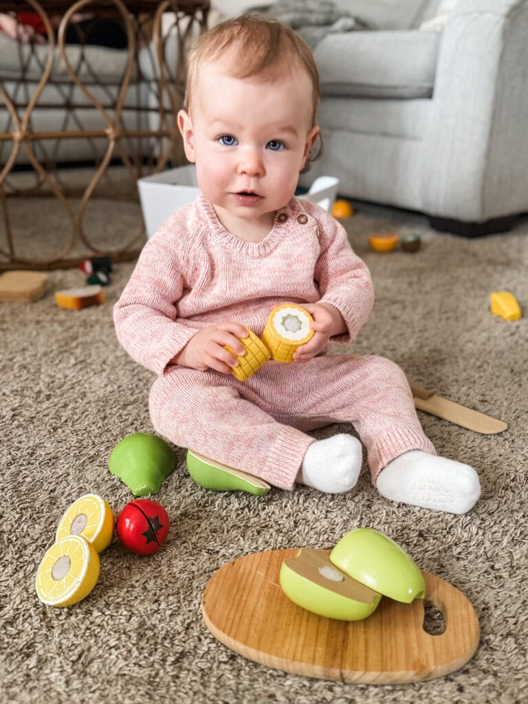 Toddler playing with wooden fruit cutting set sensory toy for toddlers.