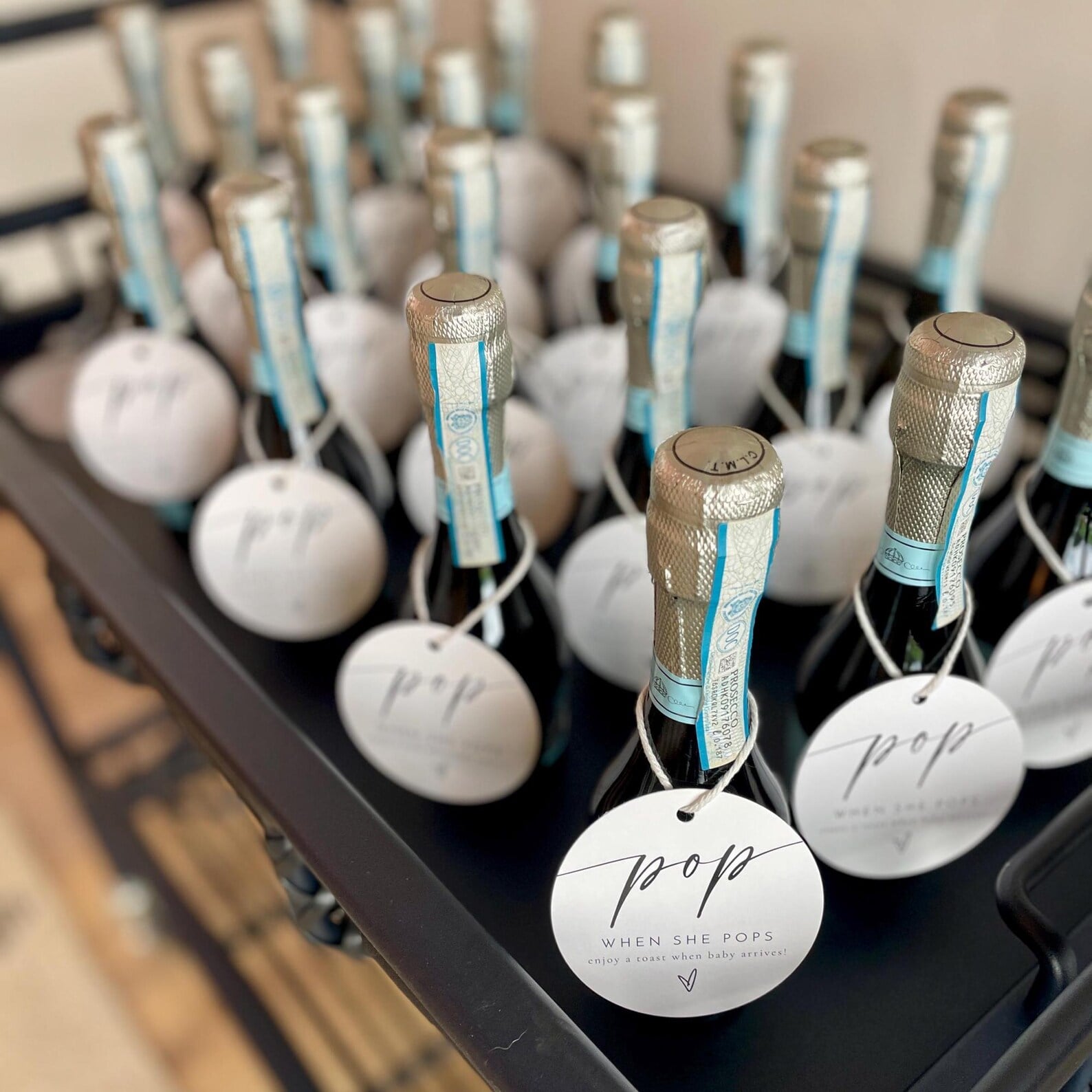 Mini champagne bottle with “pop it when she pops” baby shower party favor tags.