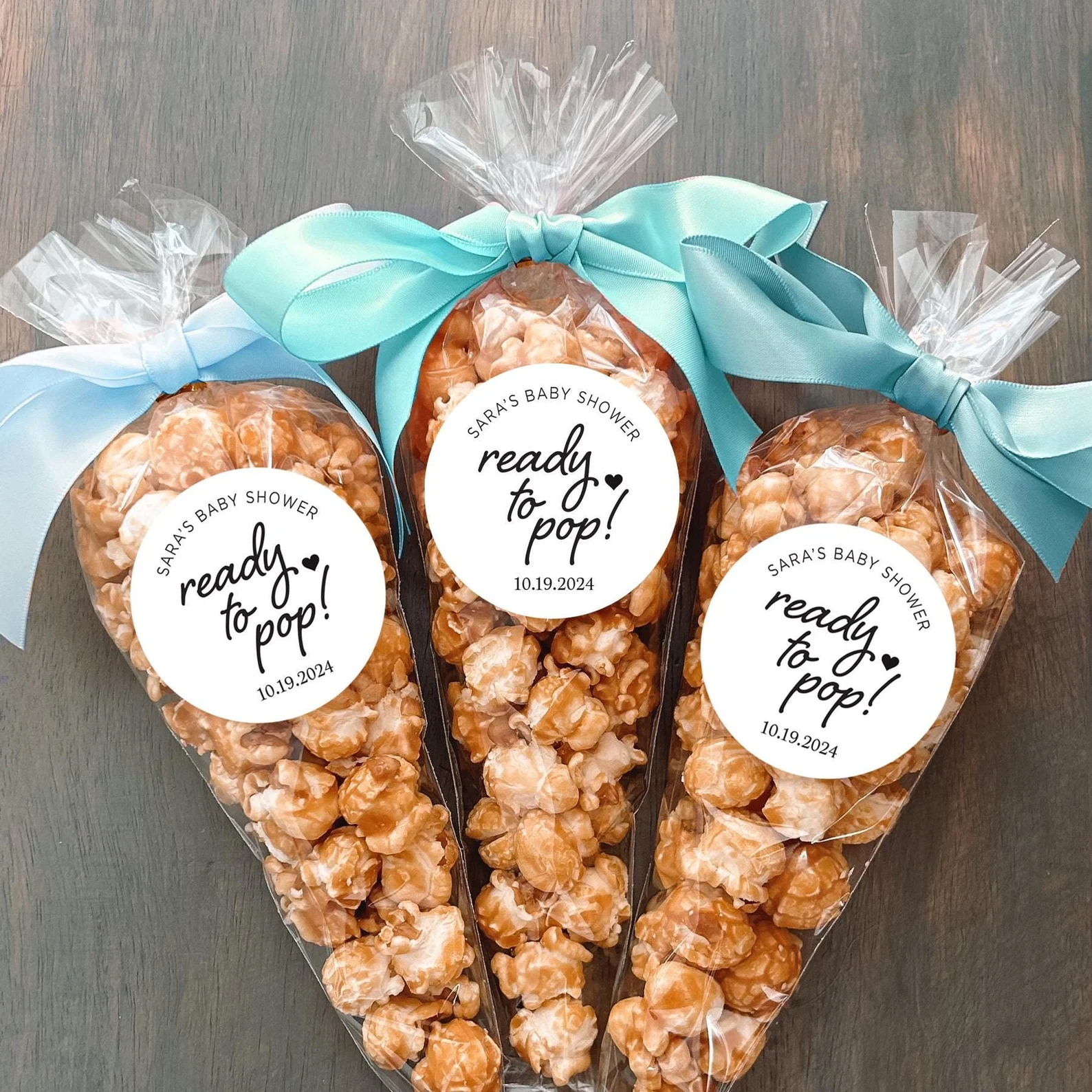 Baby shower party favor bags filled with popcorn, with custom labels and ribbon bows.