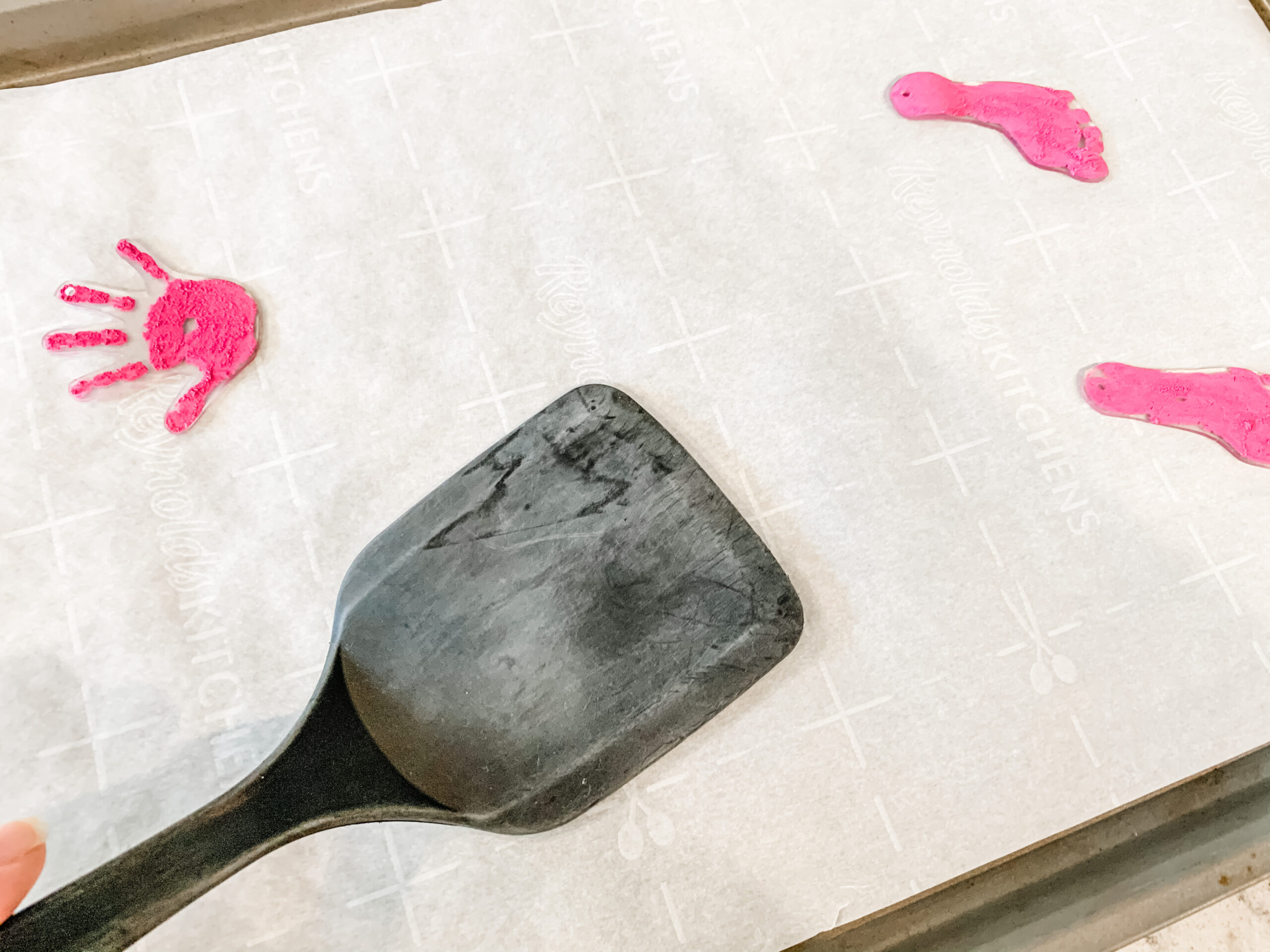 Shrink plastic keychain craft just came out of the oven. Keychains are being flattened with a plastic spatula.