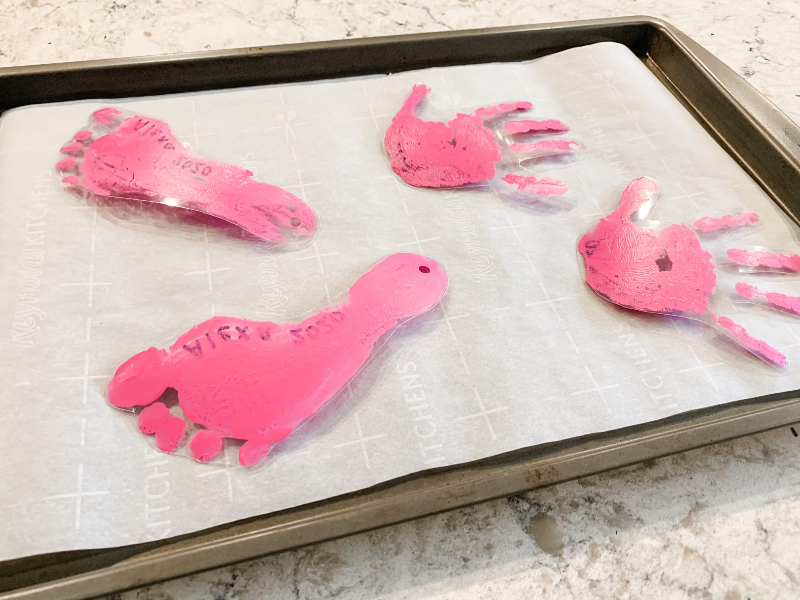Handprint keychains on parchment-lined baking sheet before shrinking