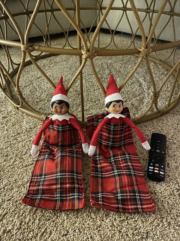Elf on the shelf in sleeping bags watching movies with the remote