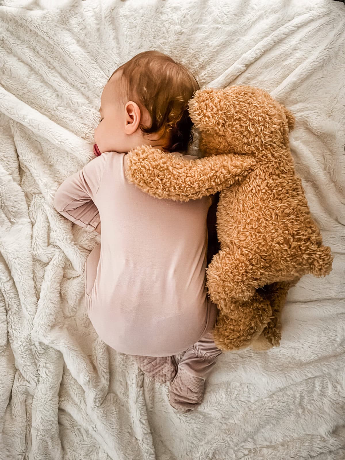 Eleven-month-old baby girl napping in her crib on a white blanket with a teddy bear positioned beside her, capturing a peaceful milestone moment.