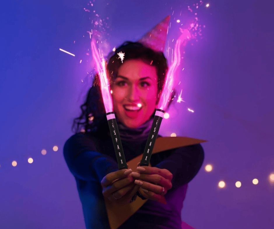 A woman smiling, holds two lit pink gender reveal sparklers.