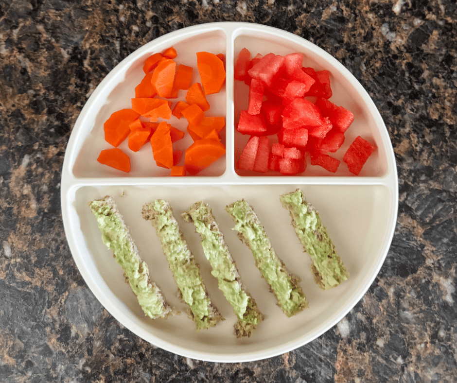A toddler lunch with avocado toast, steamed carrots and watermelon.