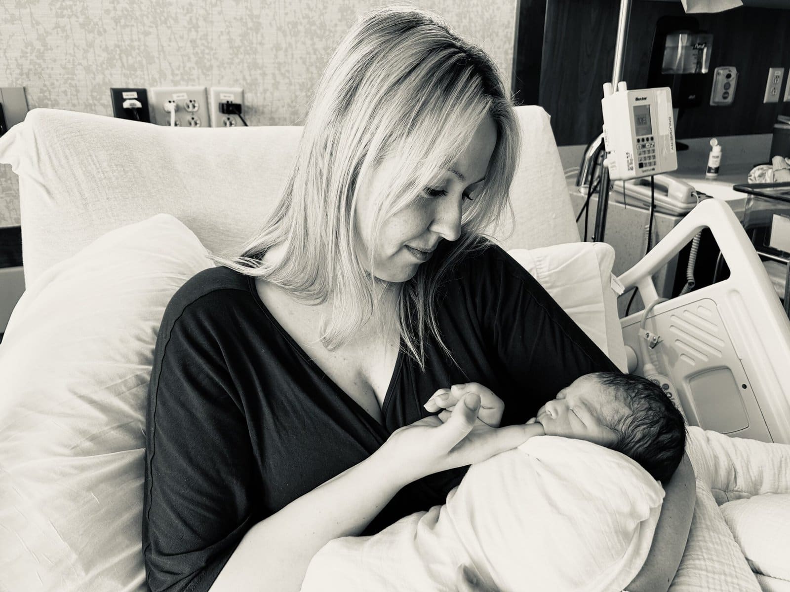 Mother holding and gazing lovingly at her newborn baby in a hospital bed, capturing an emotional first moment after birth.