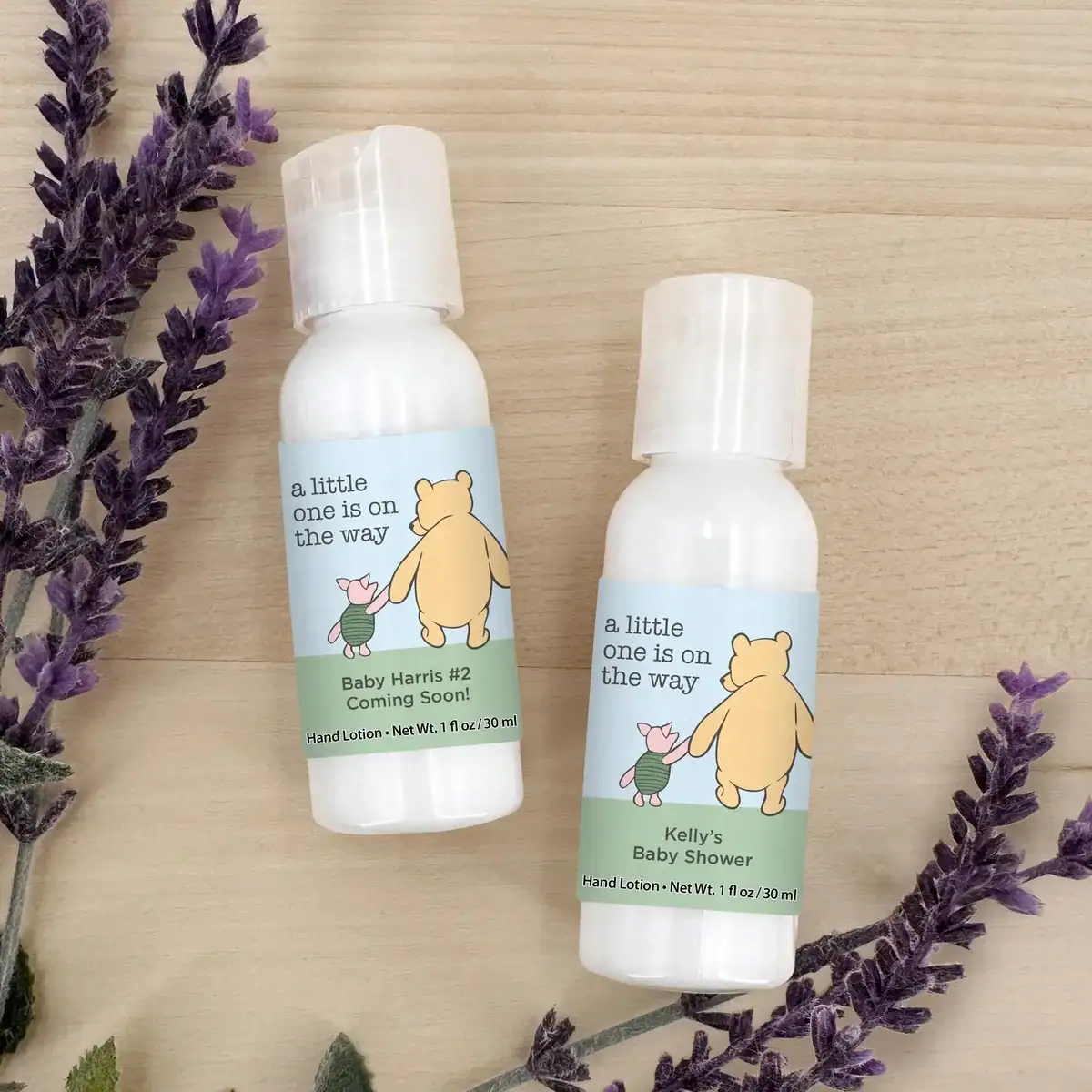 Winnie the Pooh themed baby shower lotion favors with personalized labels that say “A little one is on the way,” displayed with lavender on a wood background. Custom mini lotion bottles make cute and practical baby shower party favors for guests.