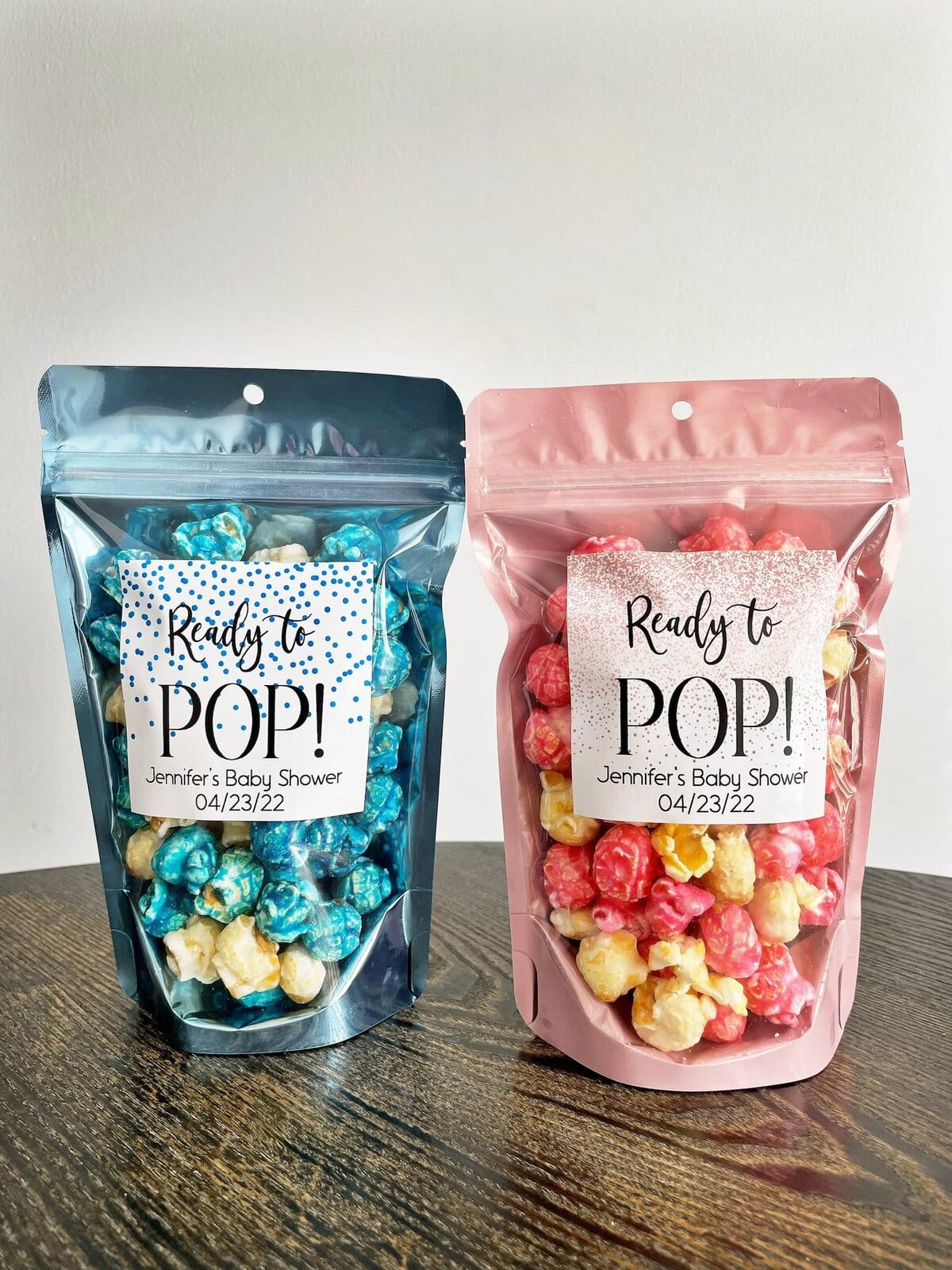 Blue and pink popcorn baby shower favors in resealable bags with “Ready to Pop!” labels personalized for Jennifer’s Baby Shower on 04/23/22 — fun and colorful baby shower party favor idea.