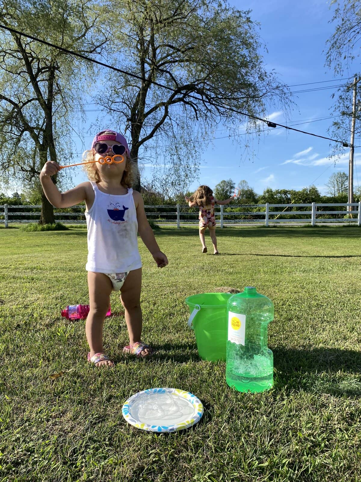 Toddler blowing bubbles into the sunlight with bubbles floating around her face