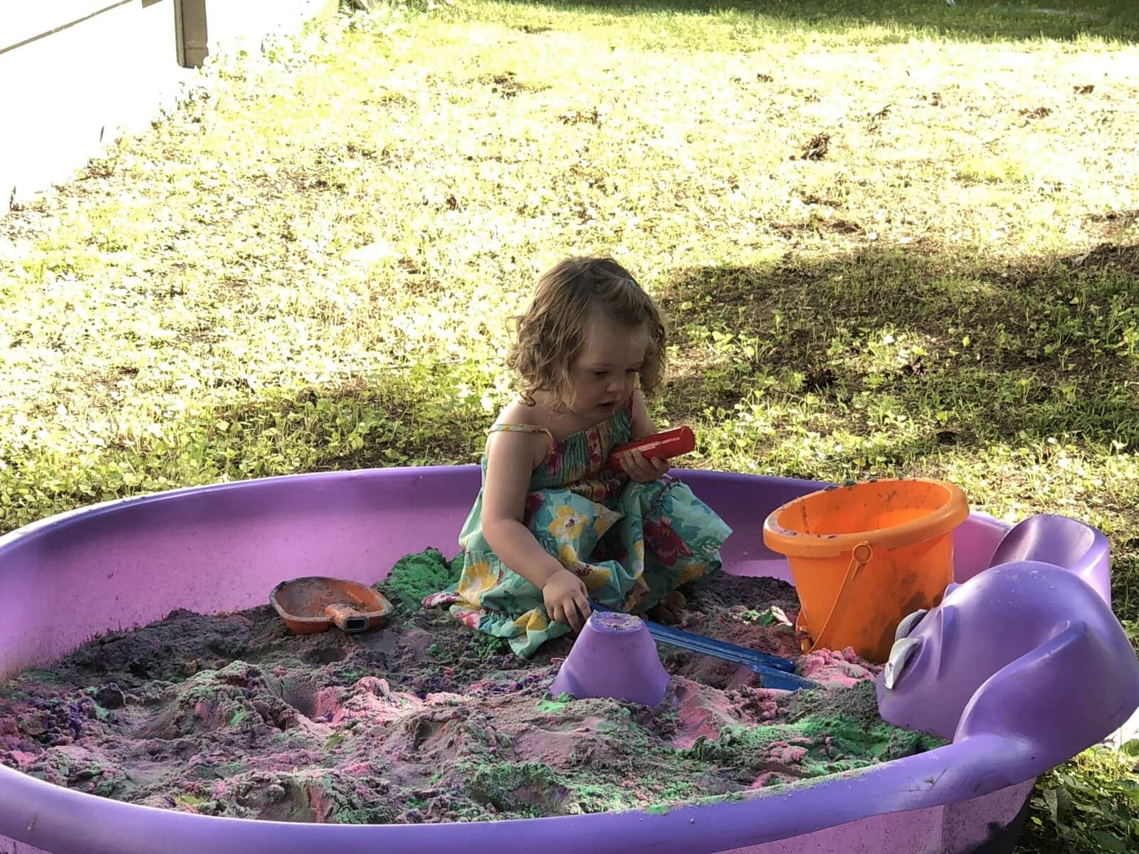 Toddler playing with colorful kinetic sand and beach toys inside a plastic kiddie pool outdoors