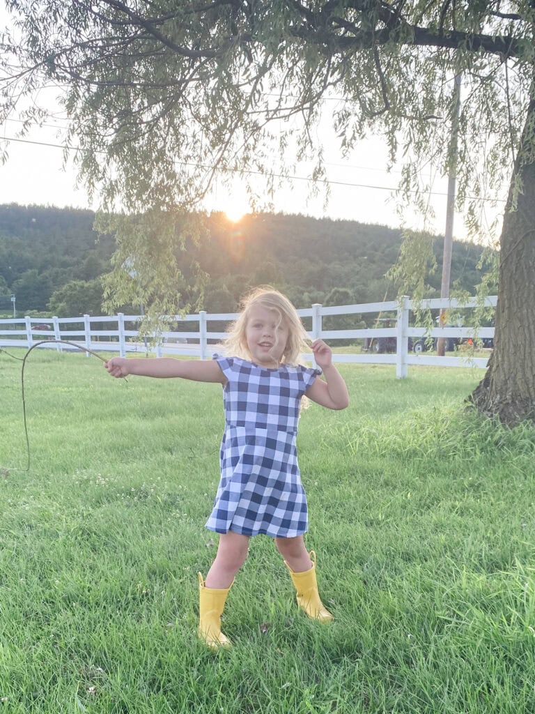 Child wearing a dress and holding a wand, playing pretend fairy princess in the yard