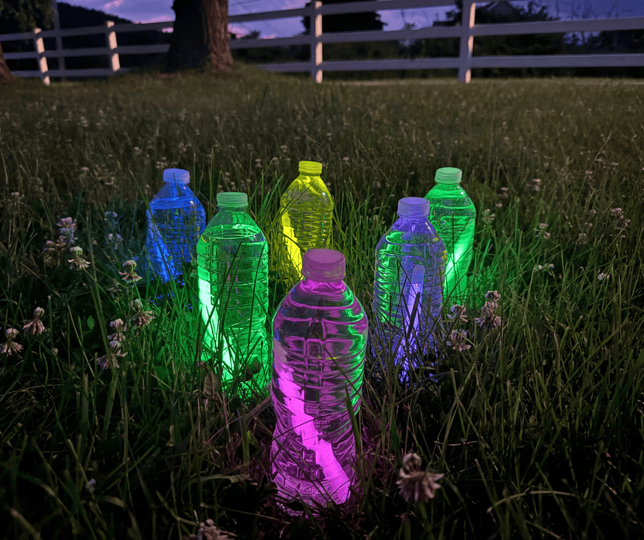 Colorful glow sticks inside water bottles arranged in the grass for a fun nighttime glow-in-the-dark bowling activity for kids.