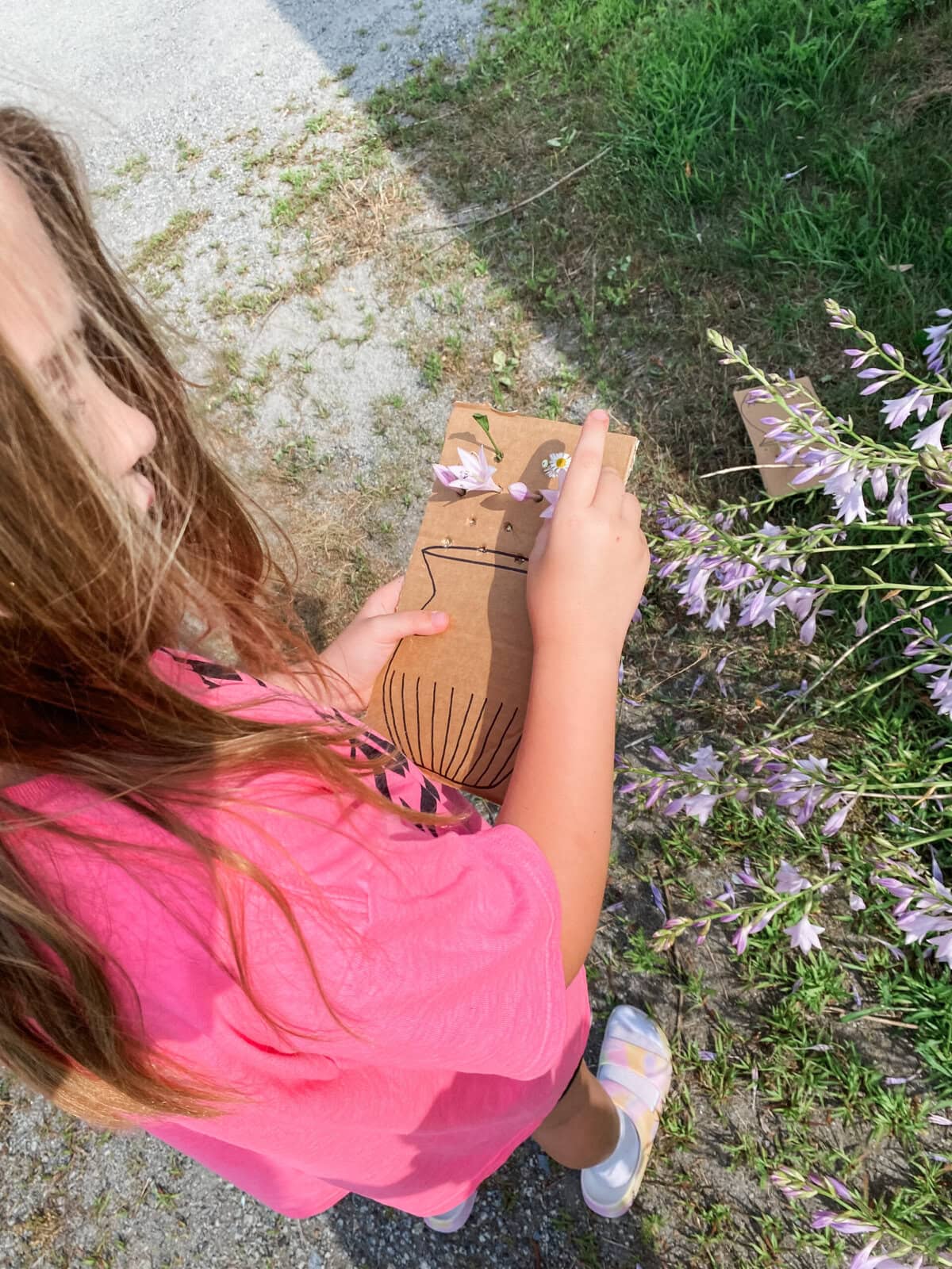 Girl placing flowers into whole on a sheet of cardboard that has a drawing of a vase on it.