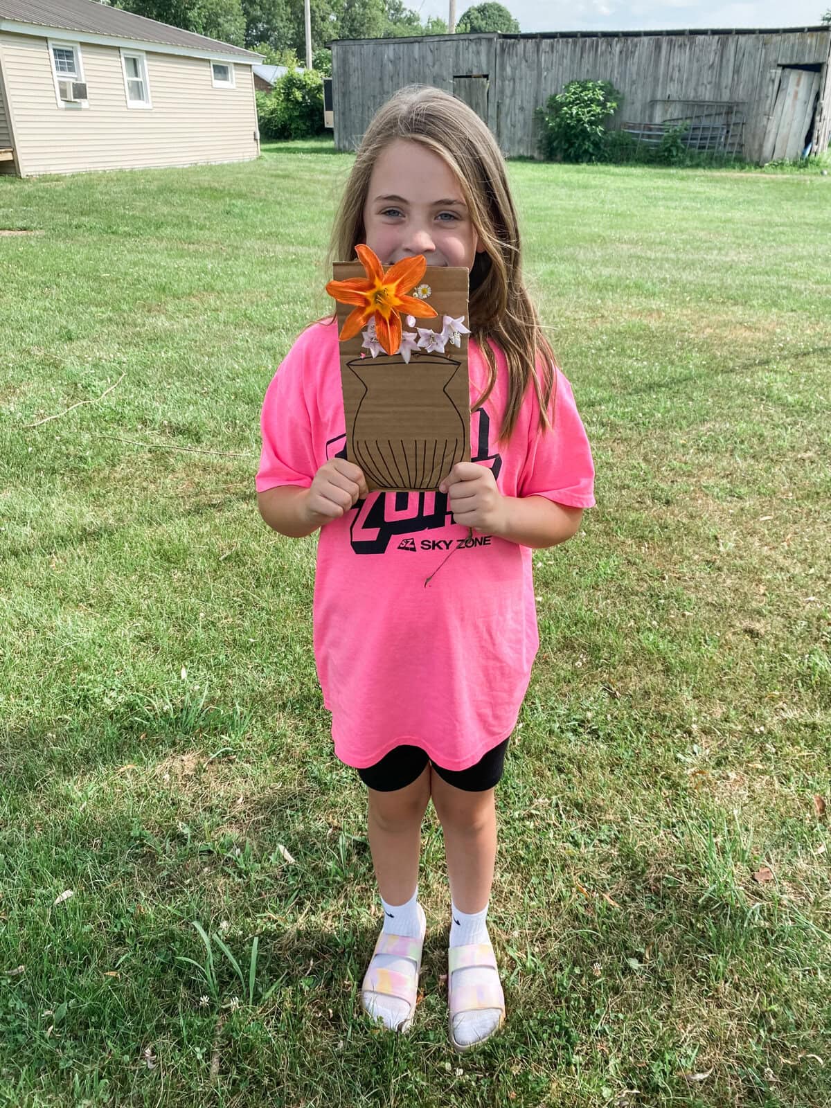 Girl proudly holding her sheet of cardboard with flowers and a drawing of a vase