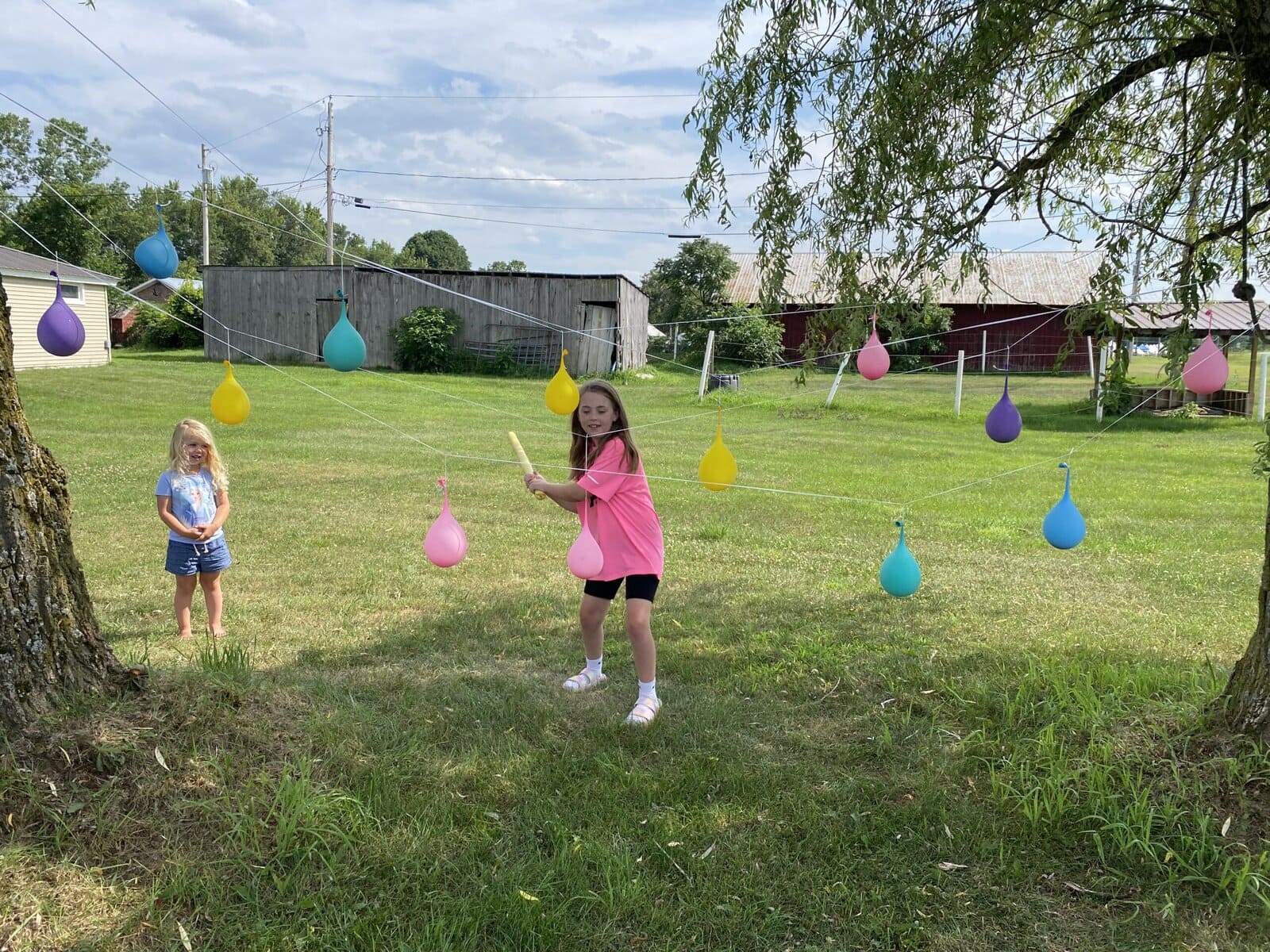 Child swinging a bat at hanging water balloons in a fun backyard summer activity for kids