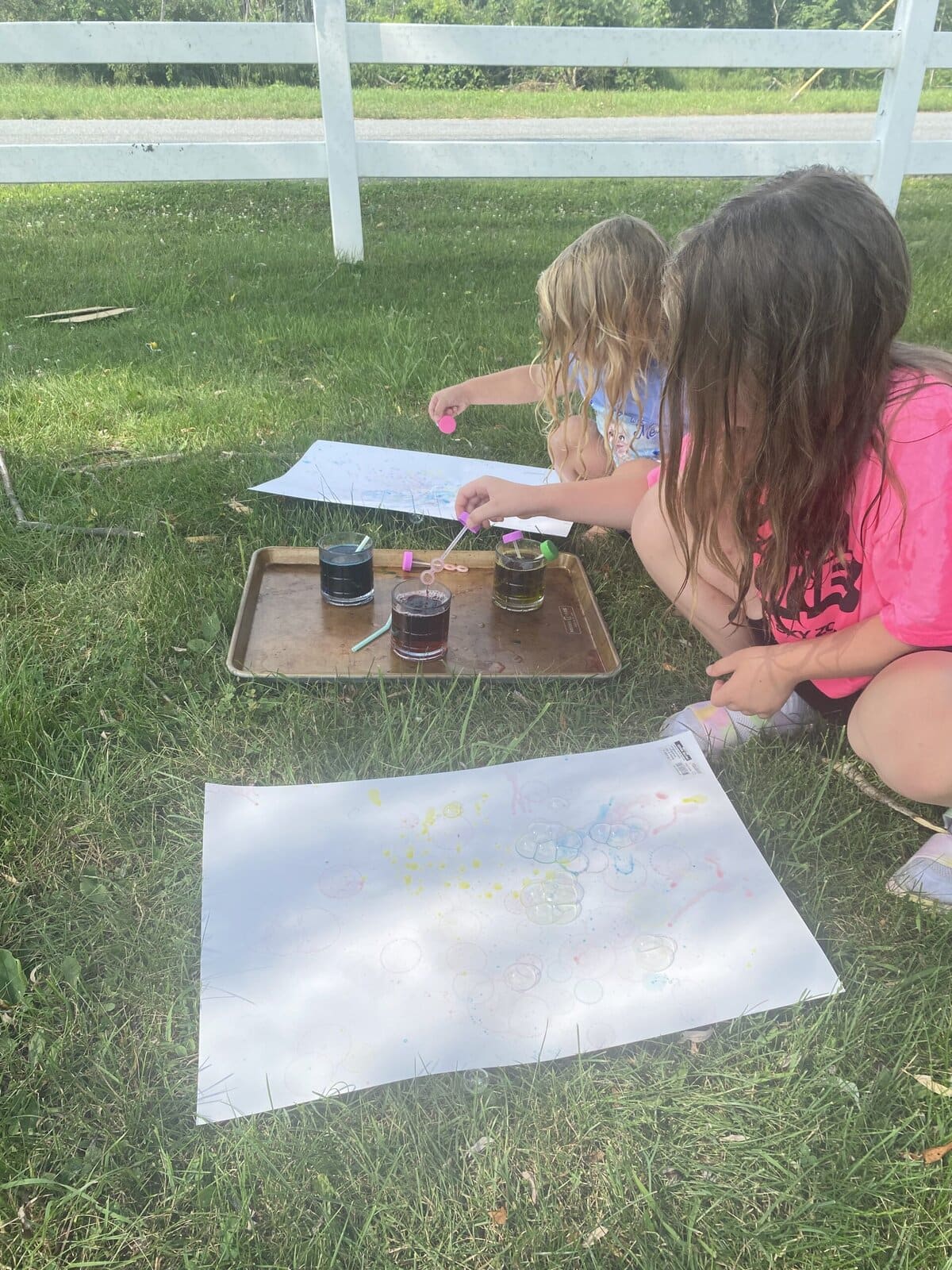 Children blowing colorful bubbles onto white paper during a creative art activity Outside during the summer.
