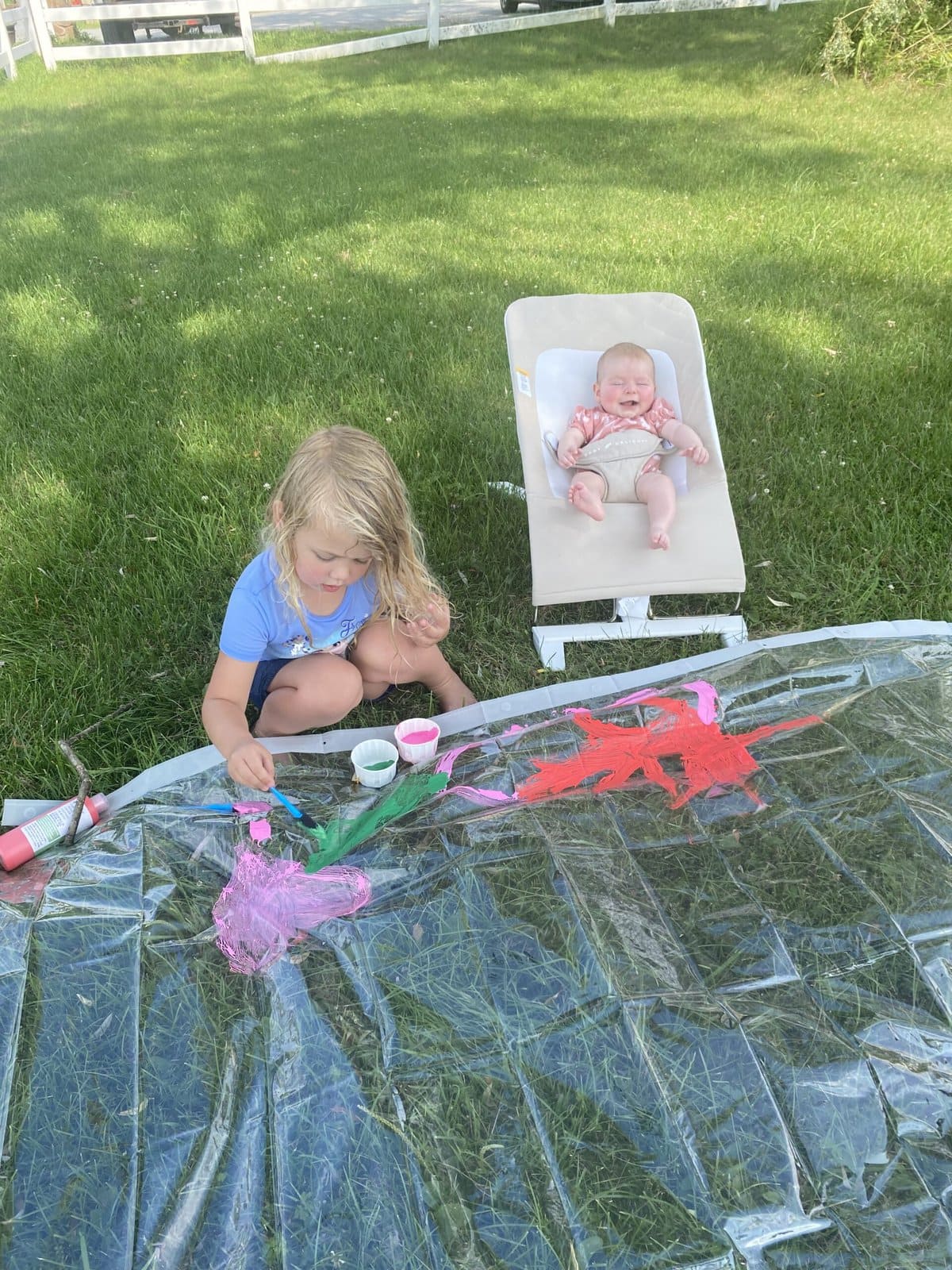 Kids painting a clear shower curtain spread across the lawn like a giant canvas
