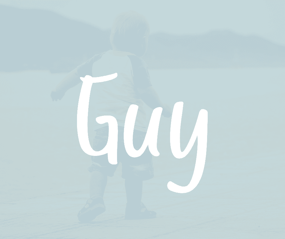 Toddler boy walking on a beach with water and mountains in the background. The name Guy is written in white over the image.