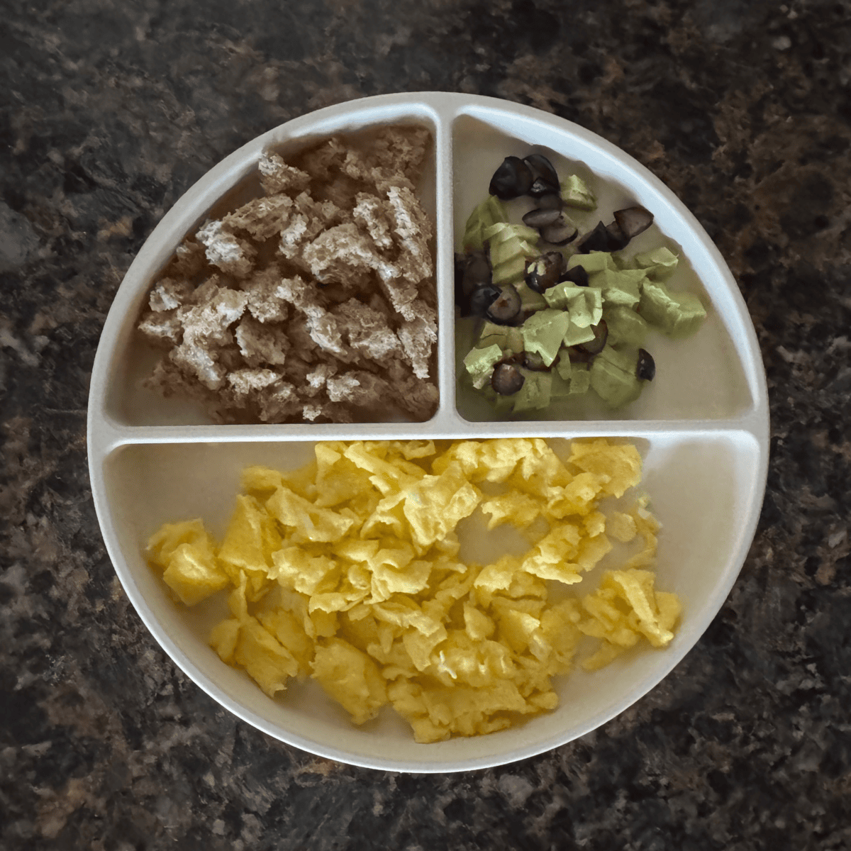 Toddler breakfast plate with scrambled eggs, diced avocado and blueberries, and soft whole wheat toast with butter — an easy and nutritious meal idea for 1-year-olds.