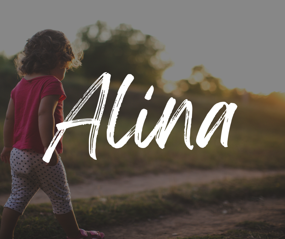 Toddler girl in a pink shirt and polka dot leggings walking on a dirt path at sunset, with the name “Alina” written in bold white script across the image.