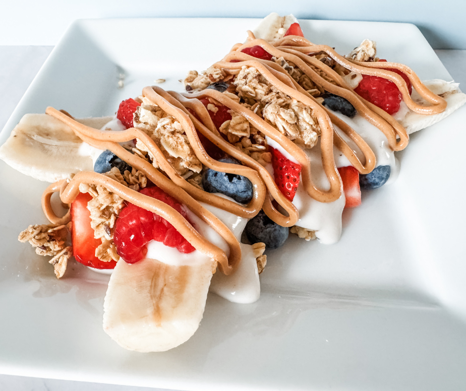 Yogurt banana split topped with berries, granola, and a peanut butter drizzle.