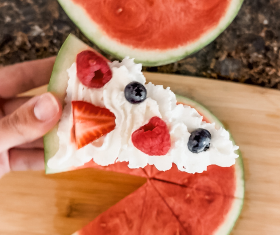 Watermelon pizza slice topped with whipped cream, strawberries, raspberries, and blueberries.
