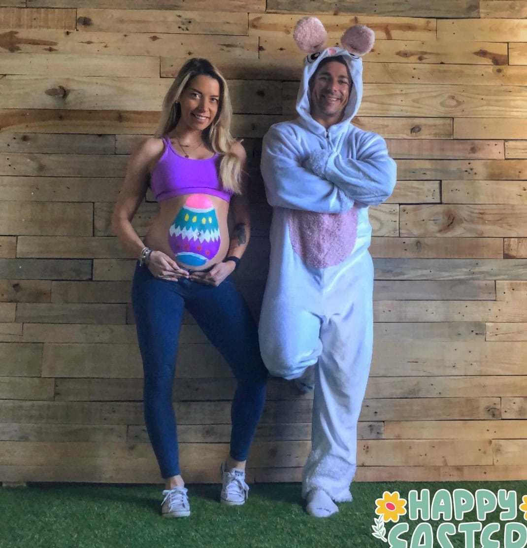 Easter pregnancy announcement photo with pregnant mom with Easter egg painted on her belly. Dad stands next to her in Easter bunny costume.