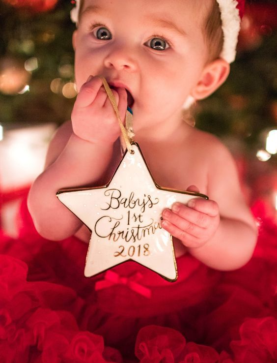 Baby holding and nibbling on a star-shaped “Baby’s 1st Christmas” ornament while surrounded by soft red tulle.