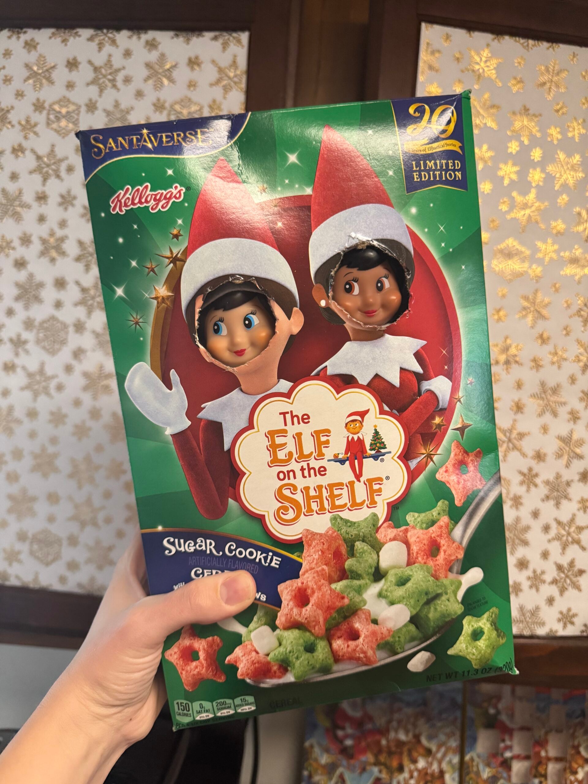 Funny Elf on the Shelf cereal box prank with two elves’ faces poking through cutout holes on an Elf on the Shelf cereal box.