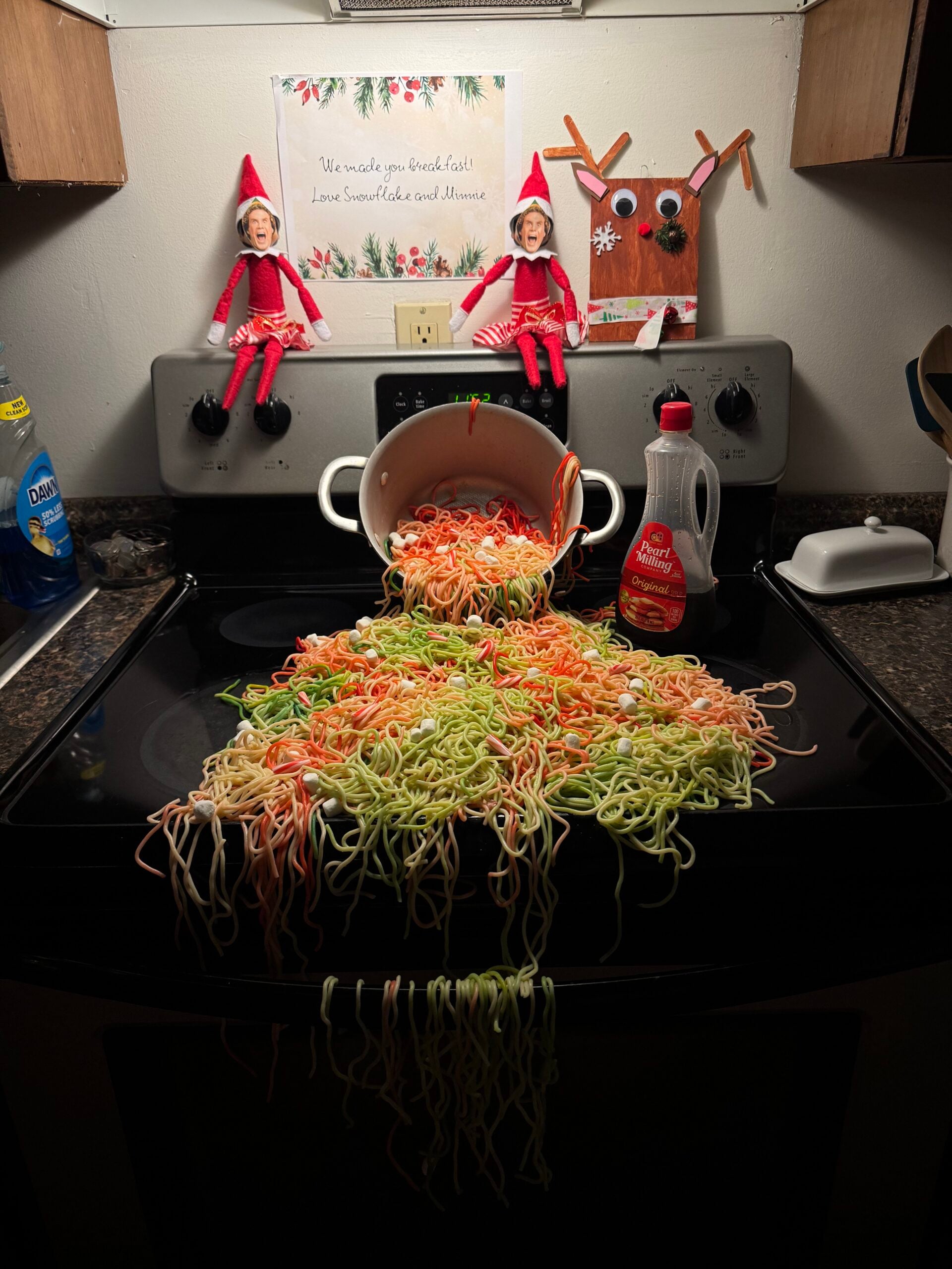 Buddy the Elf breakfast idea with colorful spaghetti, mini marshmallows and Elf on the Shelf dolls featuring Buddy’s face.