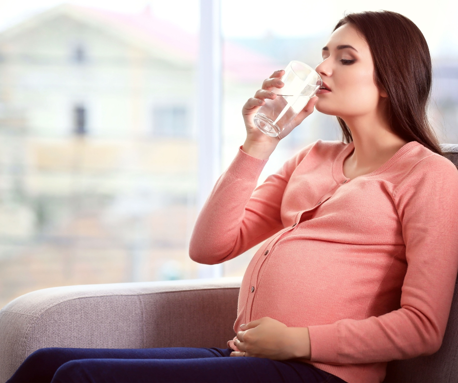 Pregnant woman sitting on a couch drinking a glass of water.