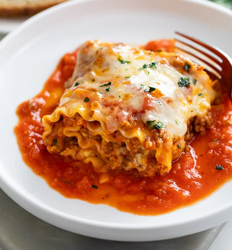 Postpartum freezer meal lasagna roll ups with meat sauce and melted cheese served on white plate