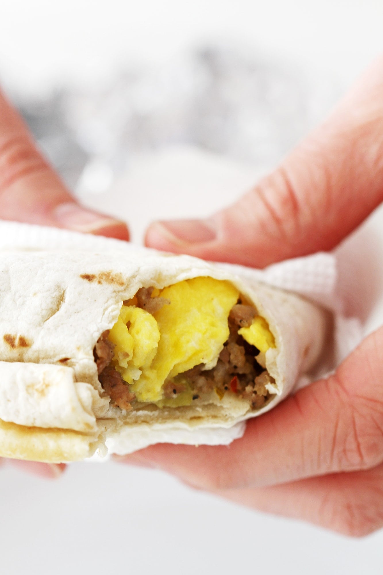 Freezer breakfast burrito with eggs sausage and cheese wrapped in tortilla being held and ready to eat