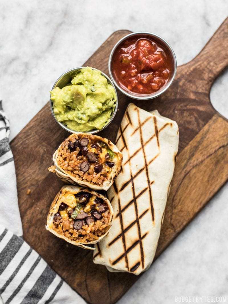 Bean and cheese burritos with rice served with guacamole and salsa on wooden board