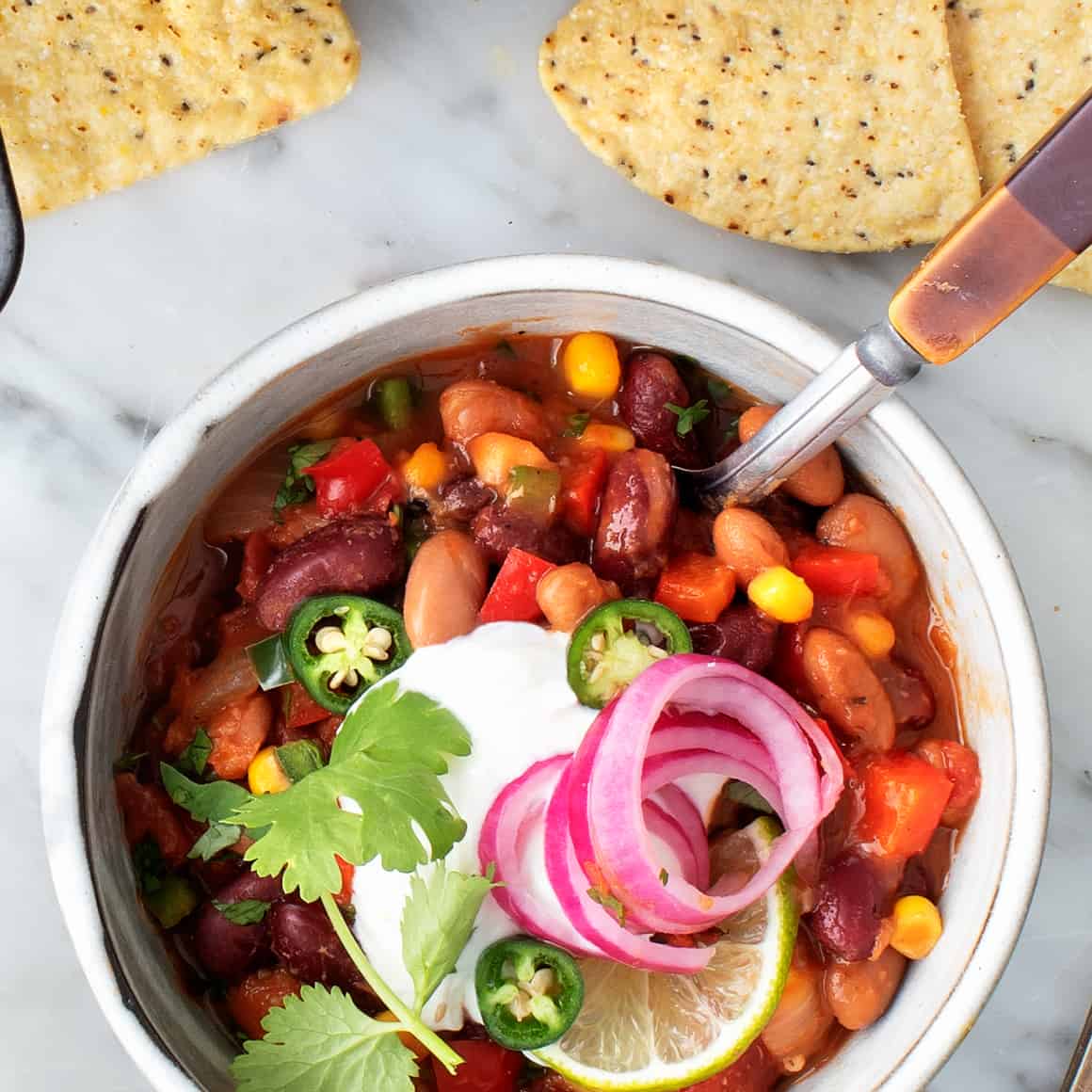 Vegetarian chili with beans corn and peppers topped with sour cream and red onion in bowl