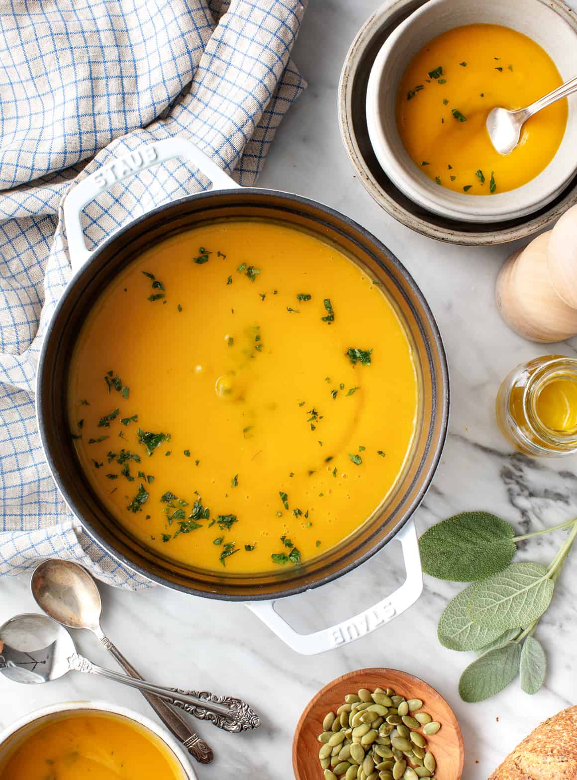 Butternut squash soup in pot with herbs served with bowl and spoon on kitchen counter