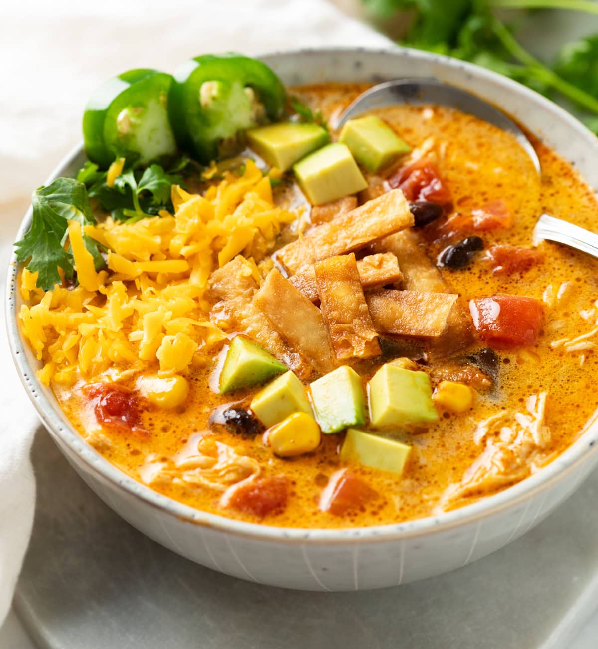 Chicken tortilla soup topped with avocado cheese tortilla strips and jalapeños in bowl.
