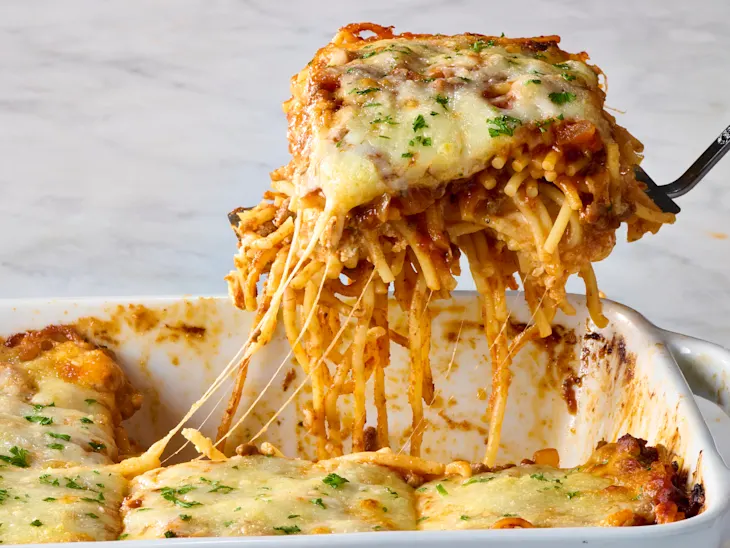 Baked spaghetti with meat sauce and melted cheese being served from casserole dish.