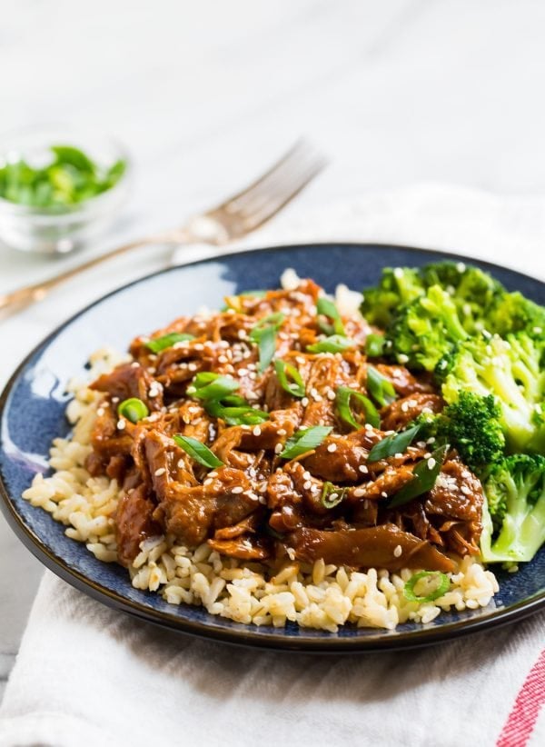 Honey garlic chicken served over rice with broccoli and green onions on plate.