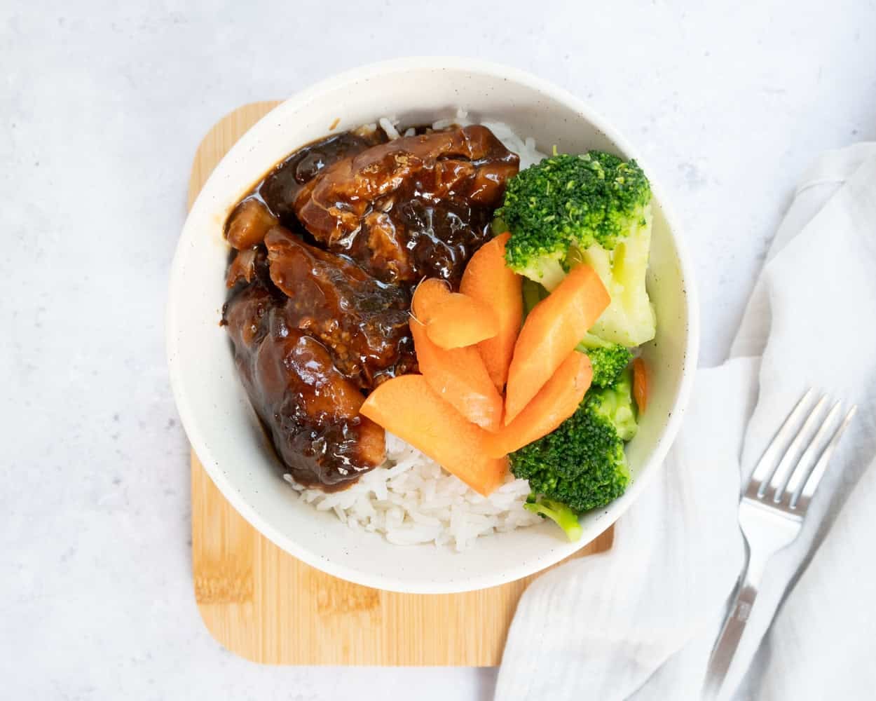 Teriyaki chicken served over rice with broccoli and carrots in bowl.