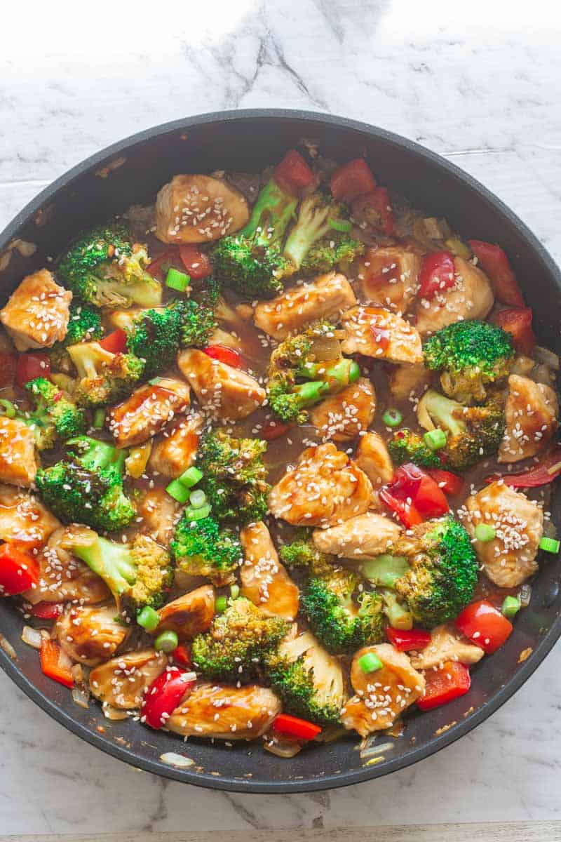 Chicken stir fry with broccoli, bell peppers, and sesame sauce in a skillet, gestational diabetes dinner idea.