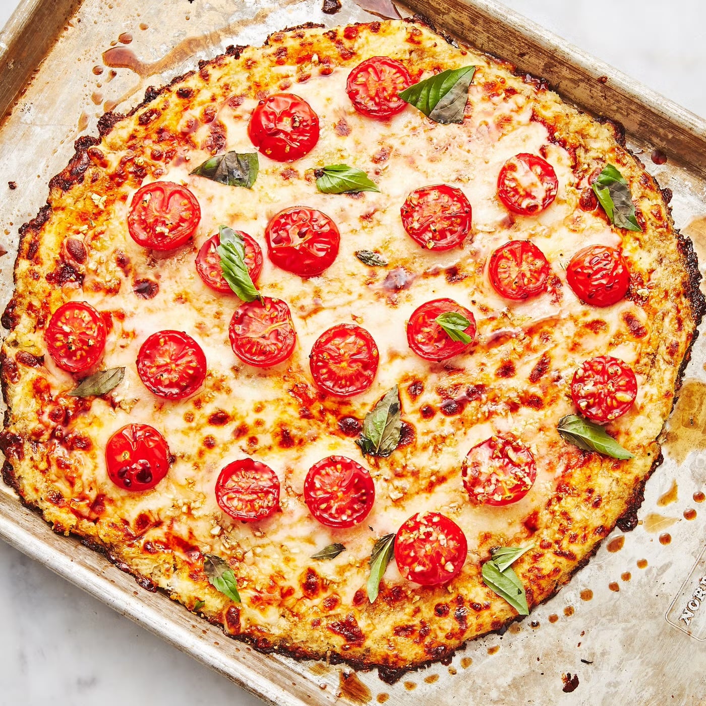 Cauliflower crust pizza with melted cheese, cherry tomatoes, and fresh basil, gestational diabetes dinner idea.
