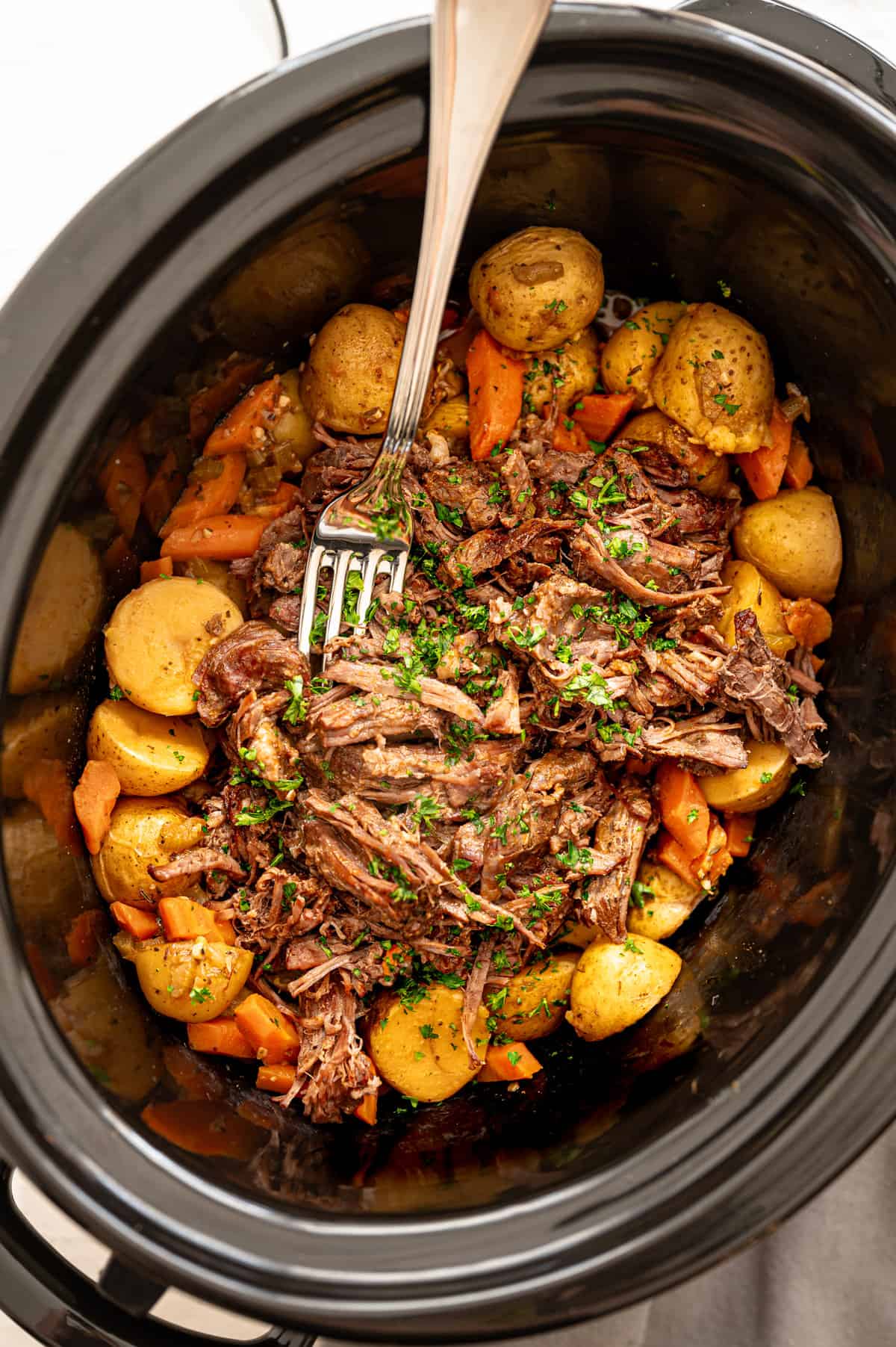 Tender crockpot pot roast with baby potatoes and carrots inside a slow cooker.