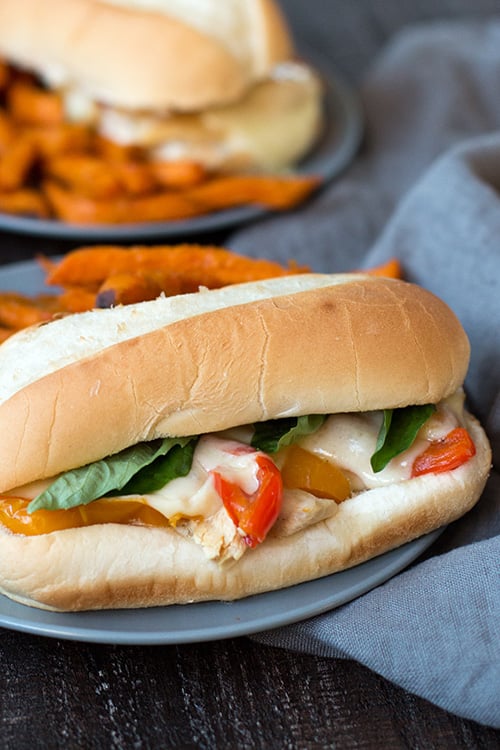 Slow cooker chicken Philly cheesesteak sandwiches topped with melted cheese and peppers served with sweet potato fries.