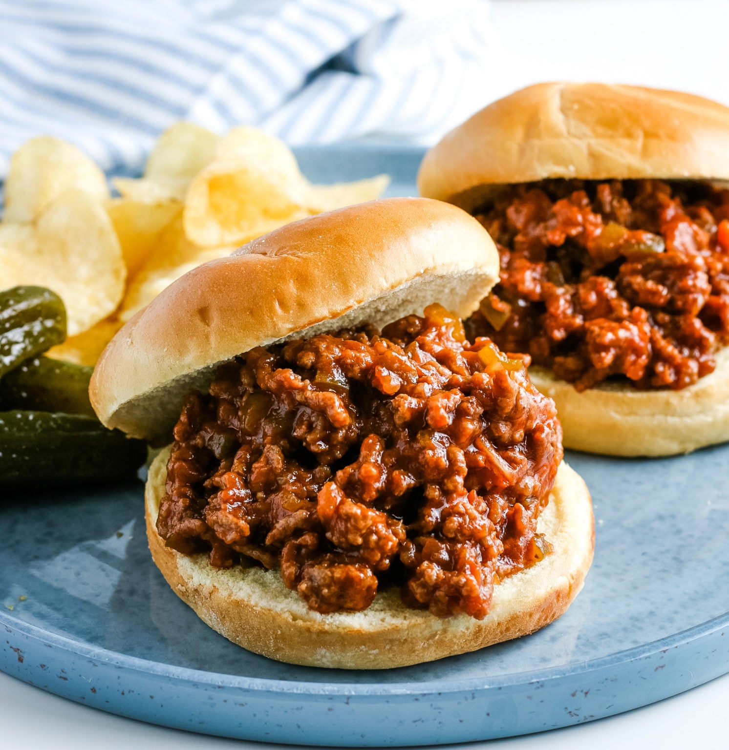 Slow cooker sloppy joe sandwiches served on hamburger buns with potato chips and pickles.